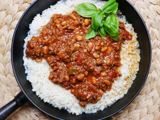 Chili con carne with rice and fresh basil in a cast iron skillet