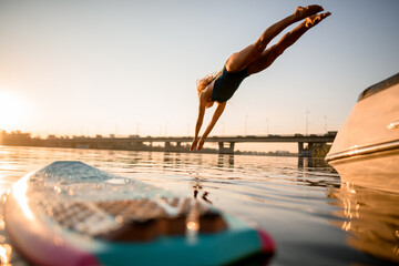 sportive woman in swimsuit jumps into the water at sunrise