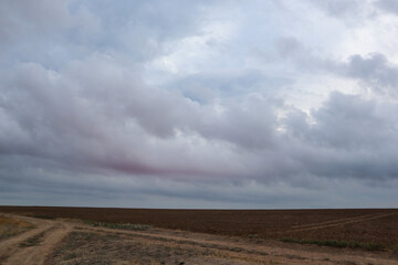 Autumn cultivated land rural bare field with dramatic sunrise sunset colored gorgeous clouds. Plowed field with grey epic cloudscape