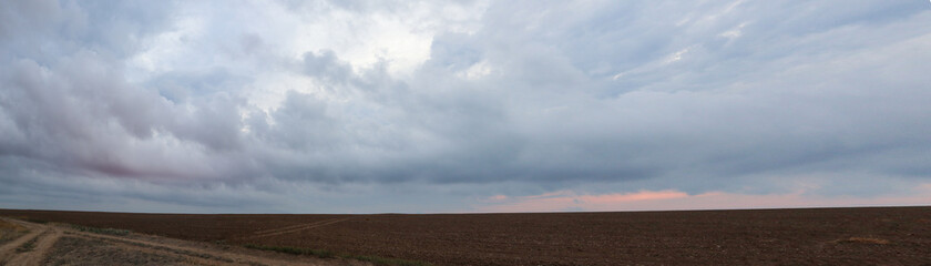 Autumn cultivated land rural bare field with dramatic sunrise sunset colored gorgeous clouds. Plowed field with grey epic layered cloudscape