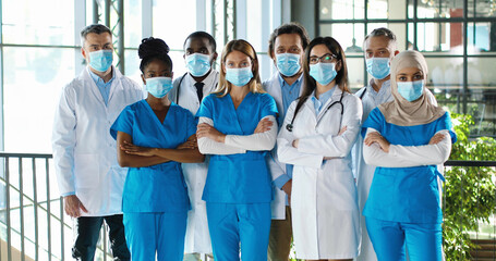 Mixed-races busy team of male and female doctors posing to camera and crossing hands in hospital....