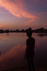 Fototapeta premium Silhouette of an Indian man standing in front of the lake during the sunset
