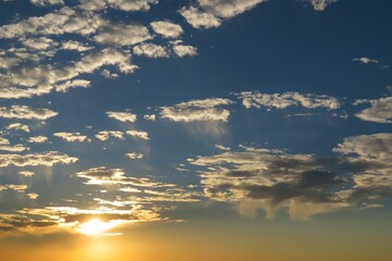 Golden sunset in blue sky with white fluffy clouds, natural background