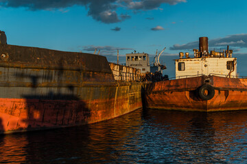 Old rusty red brown barges at sea, reflected in blue water in sunset light. Beautiful seascape with abandoned boats. Shadow