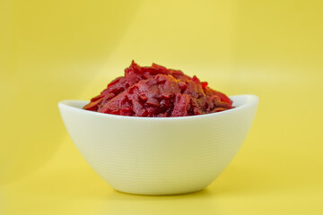 Grated beets. Fresh beet salad in white bowl isolated on yellow background. Healthy food concept, diet, fresh vegetables, vitamins and liver recovery.