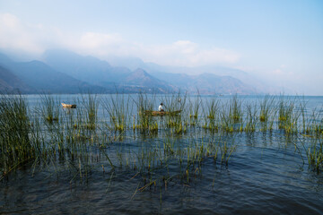 Canoe with fisherman behind reed with misty mountains at Lago Atitlan, San Juan la Laguna,...