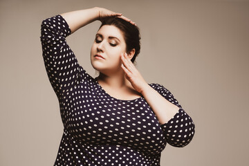 Plus size fashion model in polka dot dress, fat woman on studio background