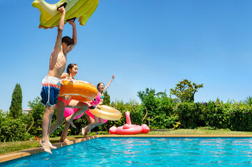 Happy boys with girls, kids holding inflatable toys dive into the water pool during summer outside