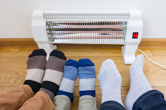 Young family warms his frozen legs near a heating radiator. Infrared halogen electric heater at home. 
