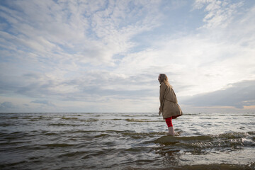 Fototapeta na wymiar pretty girl walking on a beach in beige trench coat from behind