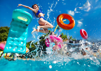 Girl in a group of teenage children have fun in the swimming pool diving with inflatable toys...