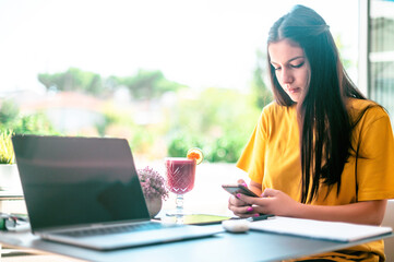 Female freelancer connecting to wireless via smart phone while having a juice in modern cafe...