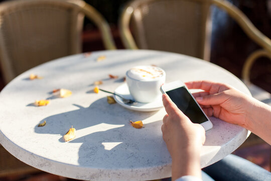 Senior Woman With Mobile Phone In Autumn Cafe Outdoors. Retired Person Using Modern Technology And Paying Online. Close Up Of Female Hands With Digital Device.