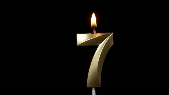 Burning birthday golden candle isolated on black background, number 7	