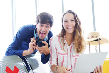 Smiling Young Caucasian traveler couple love is relaxing with camera and laptop for online social media together in the airport. Honeymoon trip on vacation concept.