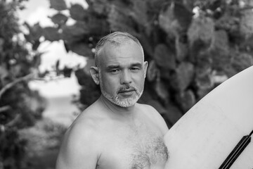Black and white portrait of handsome shirtless man surfer, holding white surf board  and cactus on background