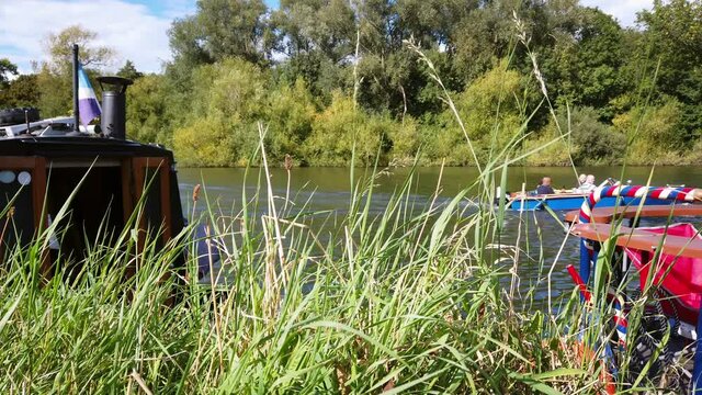 Small motor boat cruising along the River Thames - grassy foreground, 4k footage