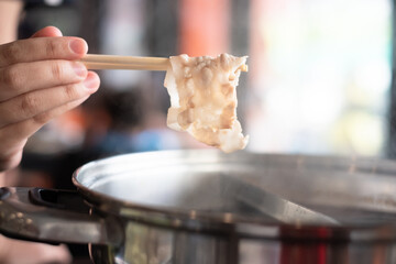 Hand holding chopsticks with ripe bacon in Shabu Shabu and Sukiyaki hot pot