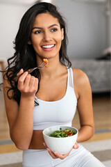 Fit woman eating healthy salad after working out at home