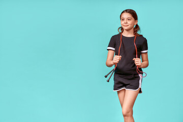 Being active. Cute teenage girl in black sportswear with jumping rope looking away and smiling...