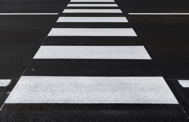 Front view of the pedestrian crossing, asphalt road, white stripes on a dark gray background, zebra...