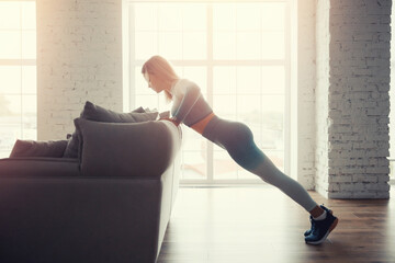 Slim sporty athletic girl does push-up exercises with improvised sofa objects at home. Concept Lifestyle sports for pandemic