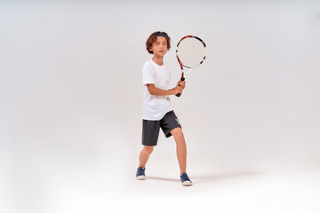 Active lifestyle. Full-length shot of a teenage boy holding tennis racket and looking away isolated over grey background