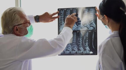 senior male doctor and surgeon woman wearing surgical face mask  Examining X-ray Report In Hospital . group of physician analyzing and discussing to bone scans during coronavirus of covid-19 pandemic - Powered by Adobe