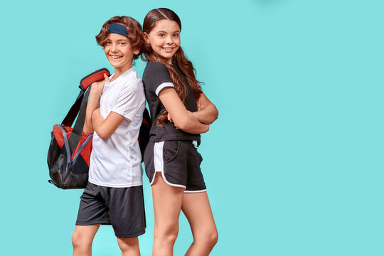 Geeting ready for training together. Two happy teenagers boy and girl in sportswear looking at camera and smiling while standing back to back isolated over blue background