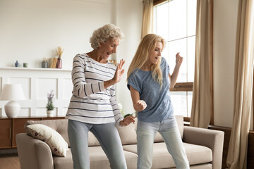 Fototapeta Improvised party. Elder and younger women best friends, aged active granny and grown grandchild girl spending time together dancing relaxing at home celebrating housewarming, purchasing new apartment obraz