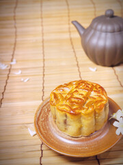 Teapot and moon cake on bamboo table. Some common jasmine orange flowers decorated.  Concept for Mid-Autumn Festival or Moon Festival, a traditional holiday in East Asia.