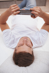 Vertical top view shot of a young manusing his smart phone, lying in a bed