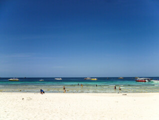 Fototapeta na wymiar The shore of the Andaman Sea in Thailand with swimming tourists and boats waiting for them.