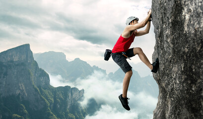 Asian man rock climber in black pants climbing on the cliff. - obrazy, fototapety, plakaty