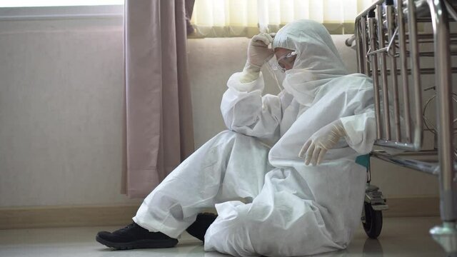 tired doctor wearing ppe suit take a break near bed after hard work feeling worry and sad  in operating room at hospital. exhausted and desperate  surgeon of Coronavirus pandemic  of covid 19 outbreak