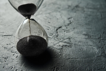 Hourglass on dark background, closeup. Urgency and running out of time concept