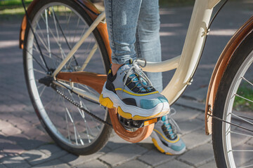 Feet shod in bright sneakers stand on the pedals of a beige bicycle