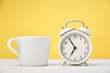 White retro alarm clock and cup on yellow background. Morning time concept