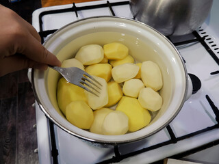 Raw potatoes are cooked in water. Cooking potatoes in a pot. Test readiness with a metal fork.