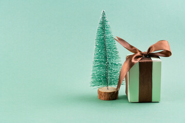 The green gift box with brown ribbon next to the Christmas tree on turquoise background . christmas concept. postcard.