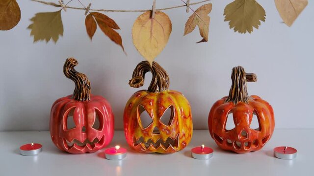 Ceramic Jack O Lanterns, burning candles and autumn leaves garland on table wall background. Home decoration. Windy.