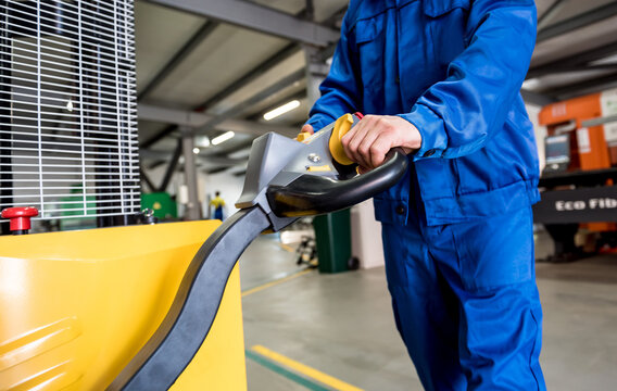 A worker in a warehouse uses a hand pallet stacker to transport pallets.