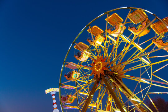 Giant ferris wheel in the background the blue sky in the evening. Amusement park at a fair with the giant vertical rotating wheel with suspended cars on the outer edge illuminated by colored lights