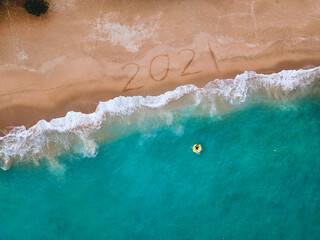 Happy New Year 2021, lettering on the beach with wave and blue sea. Numbers 2021 year on the sea...