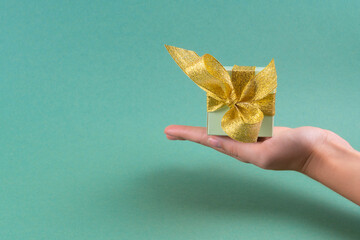 Female hands holding green gift box decorated with golden ribbon on turquoise background.christmas concept. copy spase