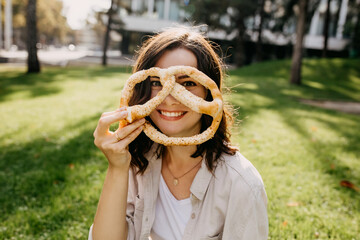 Young cheerful woman holding a pretzel, outdoors in a park.