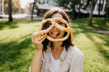 Young cheerful woman holding a pretzel, making funny face, outdoors.