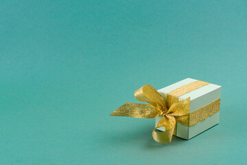 green gift box decorated with golden ribbon on turquoise background.christmas concept. copy spase