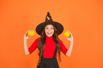 funny child in witch costume hat for Halloween with pumpkin or squash on orange background, jack o lantern