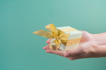 Female hands holding green gift box decorated with golden ribbon on turquoise background.christmas concept. copy spase